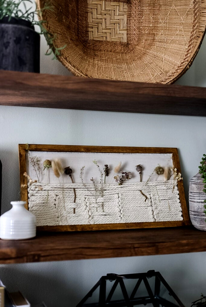 a shelf holding a botanical shadowbox, baskets, and greenery
