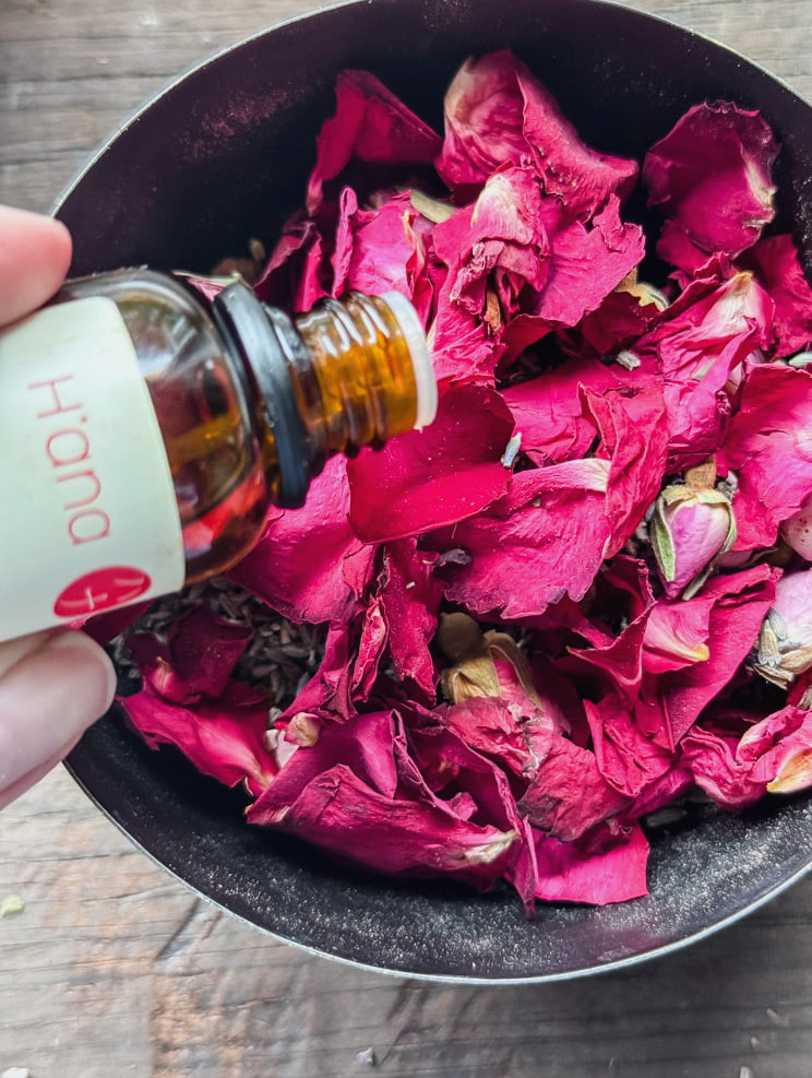 adding rose oil to a bowl of rose petals