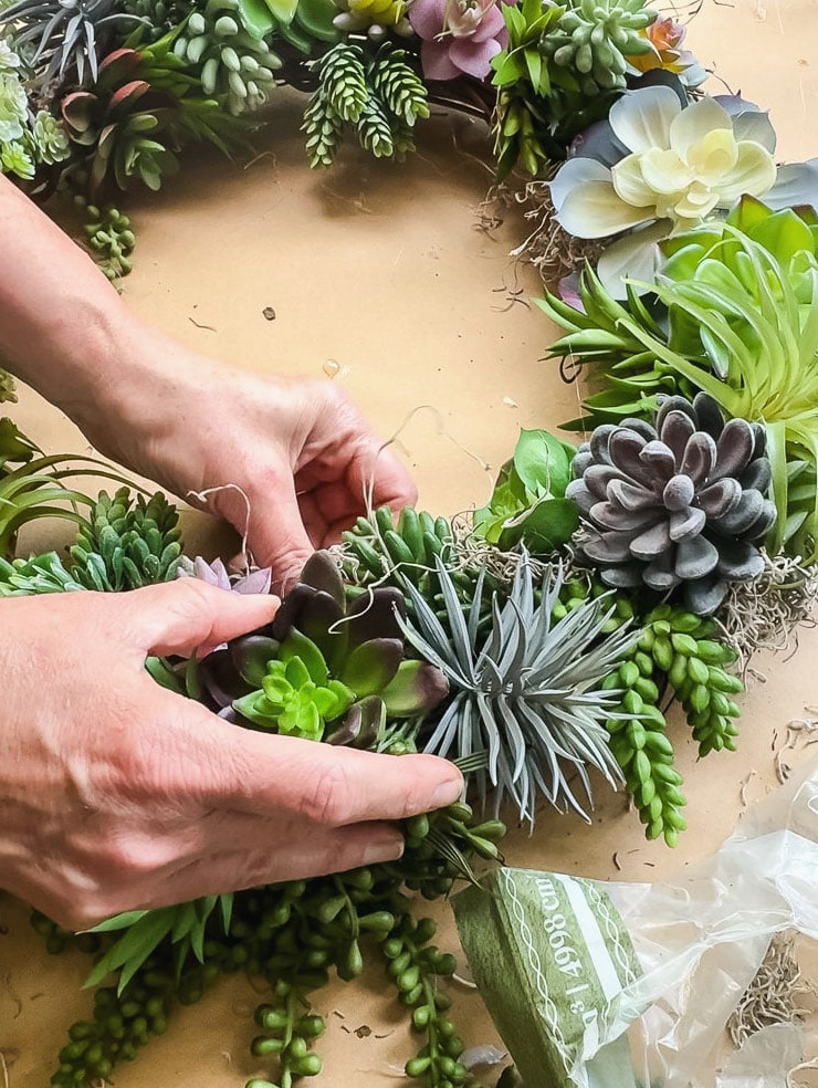 woman's hands placing spanish moss onto a diy succulent wreath project