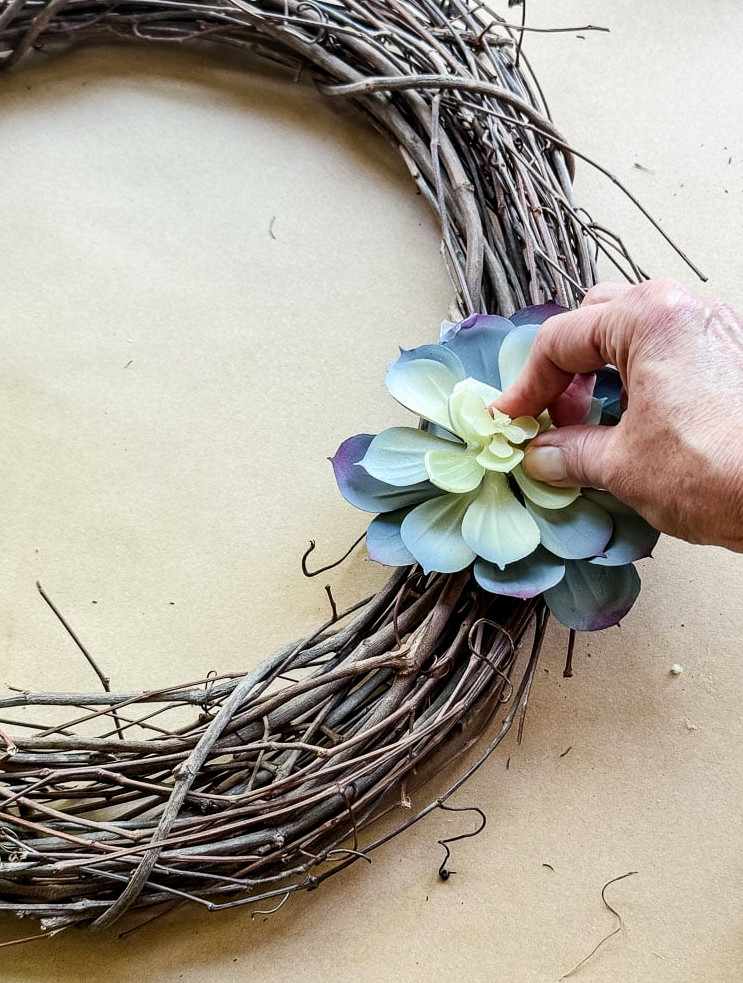 a hand gluing a faux succulent to a wreath