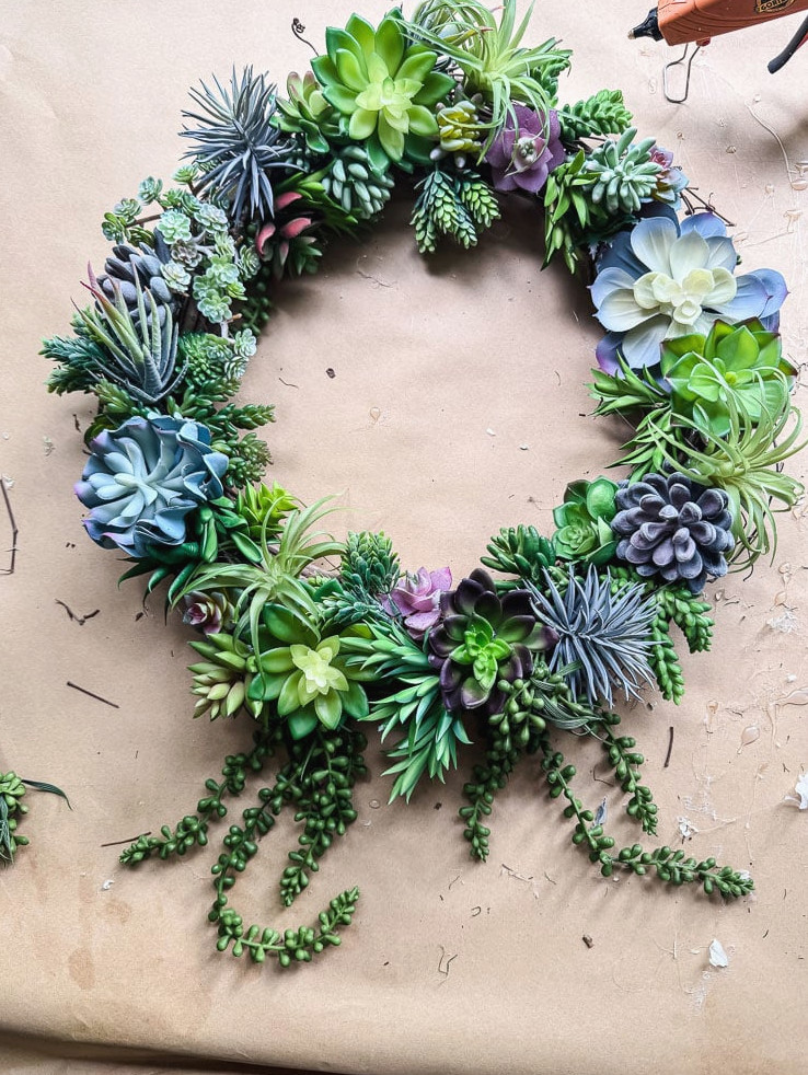artificial succulent wreath on brown kraft paper with a glue gun in view