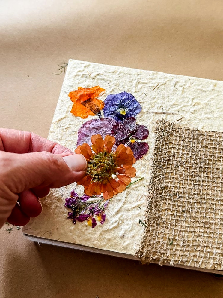 a woman's hand gluing an orange flower onto a journal cover