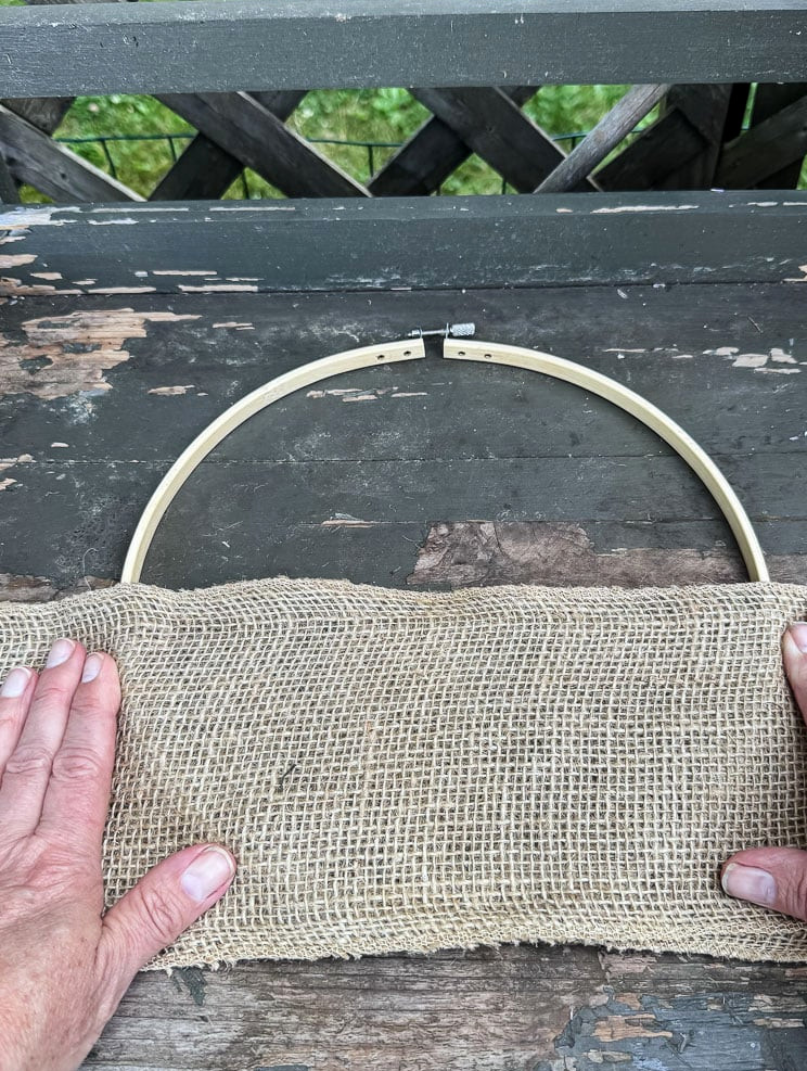 an embroidery hoop and a hand holding wide burlap ribbon on top